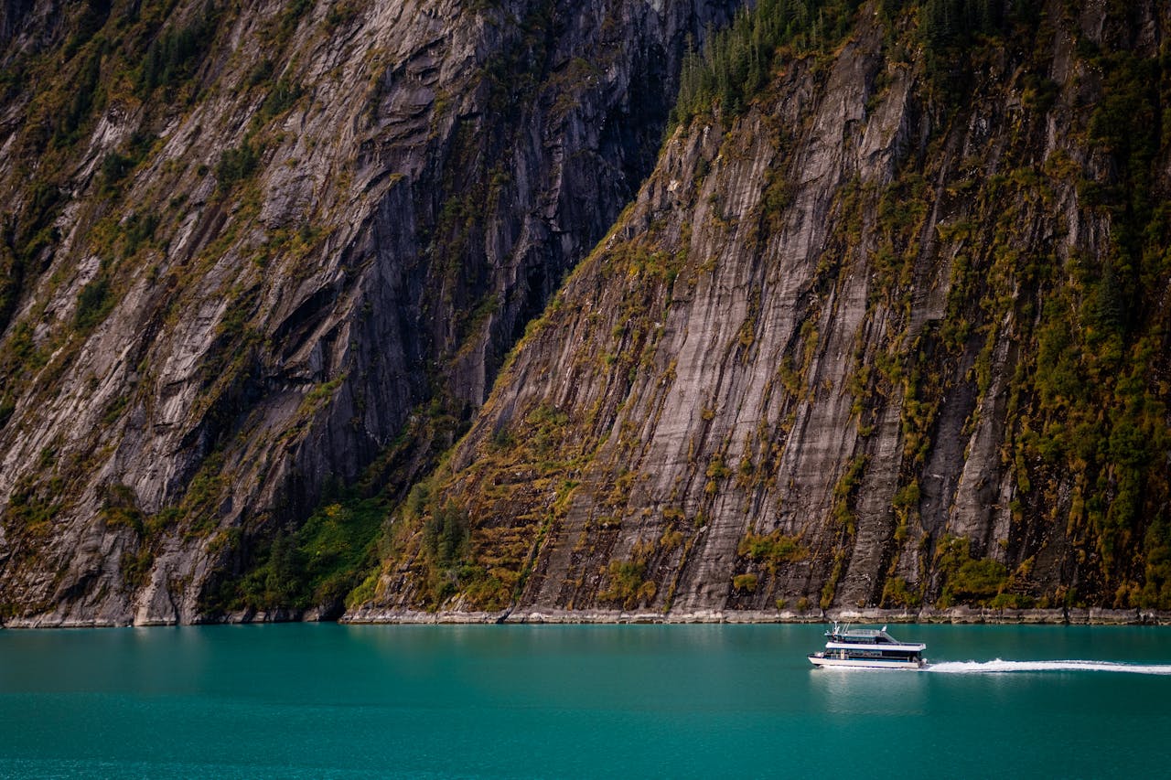 A scenic cruise boat navigates through an Alaskan fjord with towering cliffs, showcasing nature's grandeur.