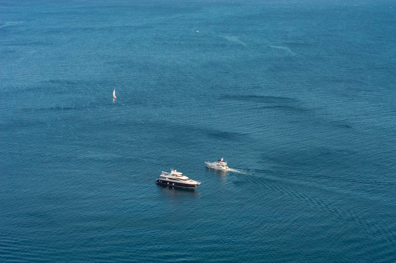 A stunning aerial view of yachts and a sailboat navigating the expansive blue sea, showcasing nautical adventure.